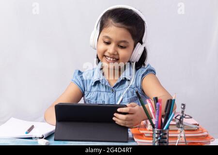 Ein hübsches indisches Mädchen, das den Online-Kurs mit Tablet und Kopfhörer auf weißem Hintergrund besucht Stockfoto