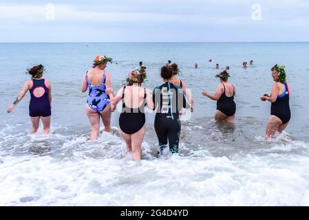 Brighton & Hove, Großbritannien. 21. JUNI 2021 Sonnenwende-Schwimmer - Mitglieder der salzigen Seevögel-Gruppe, die Blumenkronen tragen, feiern den längsten Tag bei Sonnenaufgang mit einem Bad unter bewölktem Himmel. Wetter in Großbritannien. Foto ©Julia Claxton Credit: Julia Claxton/Alamy Live News Stockfoto