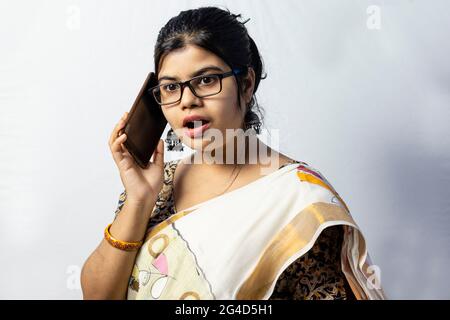 Eine schöne indische Frau im Saree, die über ein Smartphone spricht und überraschend isoliert auf weißem Hintergrund ist Stockfoto