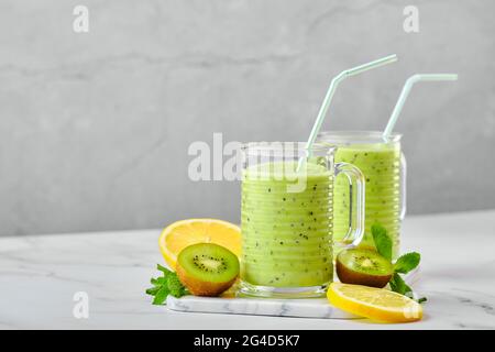Zwei Gläser mit Kiwi- und Zitronensmoothie mit Minze auf Marmorboden und Obstscheiben Stockfoto