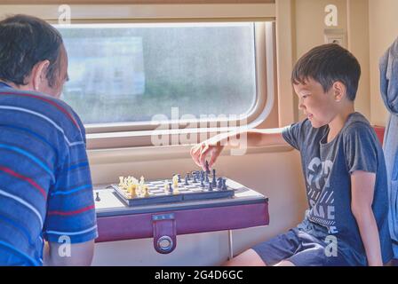 Asiatisches Kind, das mit seinem Großvater im Zug Schach spielt. Stockfoto