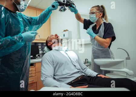 Kaukasischer männlicher Klient, der auf dem Arztstuhl sitzt und die Zähne von männlichen und weiblichen Zahnärzten untersucht hat Stockfoto