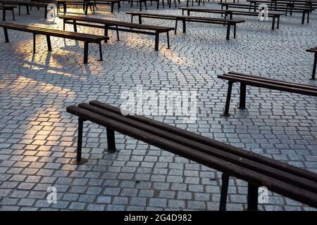 Viele Bänke in einem mit Granit gepflasterten Platz. Aufnahme bei natürlichem, weichem Licht. Ein leicht schattiger Ort. Stockfoto