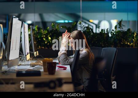 Gestresste junge Frau arbeitet im Nachtbüro Stockfoto