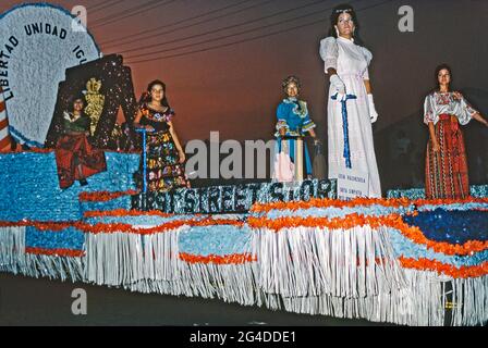 Ein Festwagen in einer Parade der Chicano-Gemeinde in Los Angeles, Kalifornien, USA, 1970 (Chicanos und Chicanas sind Männer und Frauen mexikanischer Abstammung). Der Unabhängigkeitstag (Día de la Independencia) ist ein Feiertag in Mexiko am 16. September, um die Befreiung von der spanischen Herrschaft im Jahr 1810 zu feiern. Der Float wirbt für den First Street Store. Die Frauen tragen bunte Stoffe. Dieses Bild stammt aus einer Transparenz, die von einem Amateurfotografen aufgenommen wurde und bei sehr schlechten Lichtverhältnissen aufgenommen wurde – einem alten Foto aus den 1970er Jahren. Stockfoto