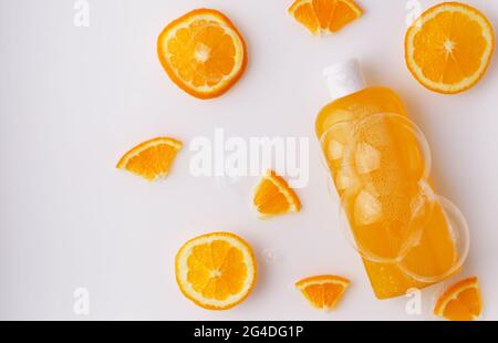 Shampoo, Duschgel, orangefarbene Flüssigseife mit natürlichen Inhaltsstoffen in einer transparenten Flasche auf hellem Hintergrund mit Blasen und orangefarbenen Scheiben Stockfoto