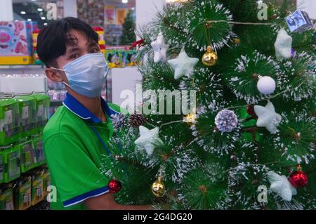 Kambodschanischer Teenager, der während der Coronavirus-Pandemie eine schützende Gesichtsmaske/Abdeckung trägt und einen geschmückten Weihnachtsbaum hält. Steung Meanchey, Phnom Penh, Kambodscha. Dezember 2020. © Kraig Lieb Stockfoto