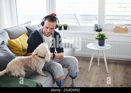 Porträt eines behinderten jungen Mannes, der zuhause mit dem Hund spielt, Beinprothetik. Stockfoto