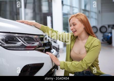 Junge schöne Frau, die ein neues Auto zum Verkauf im Autohaus ansieht Stockfoto