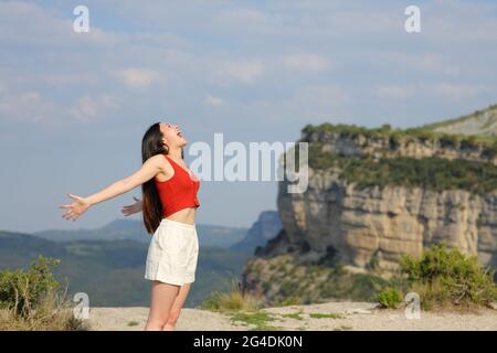 Profil einer Frau mit gemischter Rasse, die oben auf einer Klippe im Berghang in die Luft schreit Stockfoto