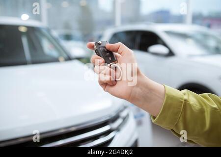 Nahaufnahme eines Autoschlüssels in der weiblichen Fahrerhand, Fahrzeuge im Autohaus im Hintergrund Stockfoto