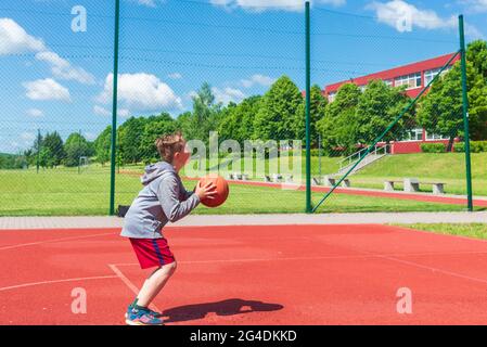 Junge Vorbereitung für Basketball-Schießen auf Playground.Boy führt Schuss bei Basketball-Spiel auf dem Spielplatz während sonnigen Sommertag. Stockfoto