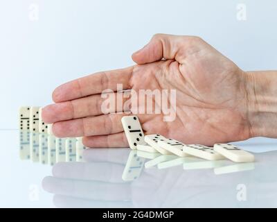 Hand stoppt Dominoeffekt auf weißem Hintergrund. Stockfoto