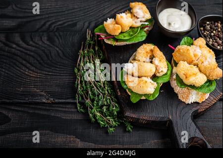 Toasts mit knusprig gebratenen Garnelen und grünem Salat auf einem Holzbrett. Schwarzer Holzhintergrund. Draufsicht. Speicherplatz kopieren Stockfoto