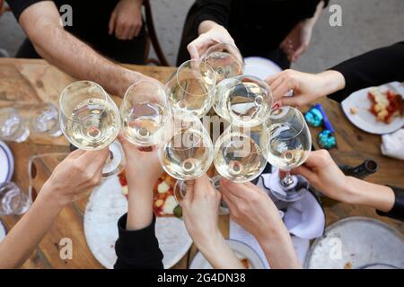 Von oben der Gruppe der Ernte anonymen Menschen versammeln sich um den Tisch mit Pizza und klirrende Gläser mit Weißwein während der Party-Feier Stockfoto