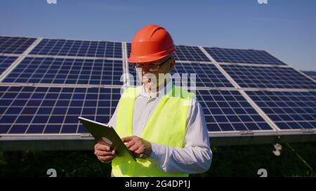 Ein junger Ingenieur überprüft mit Tablet den Betrieb von Sonne und Sauberkeit auf dem Feld der Photovoltaik-Solarzellen bei Sonnenuntergang. Konzept: Erneuerbar Stockfoto