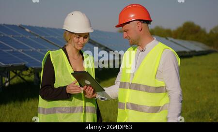 Zwei Ingenieure diskutieren die Zeichnungen für das Projekt. Sie stehen an einer Solarpanel-Station. Die Ingenieurin zeigt mit der Hand auf Stockfoto