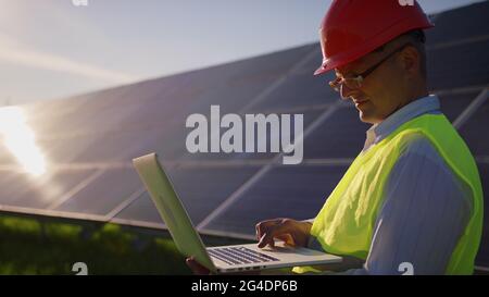 Ingenieur arbeiten Verwendung Laptop Stand in der Nähe von Solarbatterien Bau erneuerbare Energie Arbeiter Mann Technologie moderne Strom Energie Zeitlupe Stockfoto