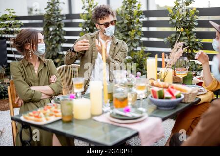 Eine Gruppe von Freunden, die Gesichtsmaske tragen, während eines Mittagessens im Freien, ein ernsthaftes Gespräch führen und während einer Pandemie Zeit miteinander verbringen Stockfoto