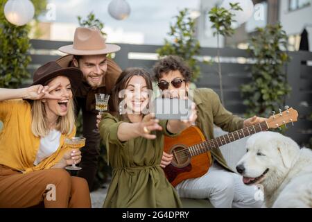 Freunde mit Getränken und Gitarre, die sich im Hinterhof amüsieren und am Telefon anrufen Stockfoto