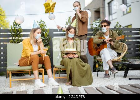 Freunde in Gesichtsmaske feiern Geburtstag im Freien Stockfoto