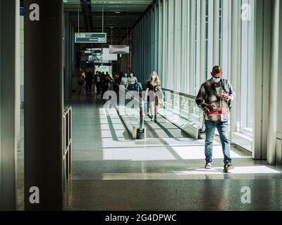 Passagiere auf dem Weg zu einem Flughafen. Die Passagiere, die alle maskiert sind, gehen auf dem Weg zum Abflugsteig durch den Flughafen. Stockfoto