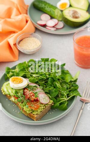 Gesundes, leckeres Frühstück, Sandwich mit Avocado und Lachs, Gurken und Radieschen sowie Mikrogemüse aus Erbsen mit gekochtem Ei und Maissalat Stockfoto