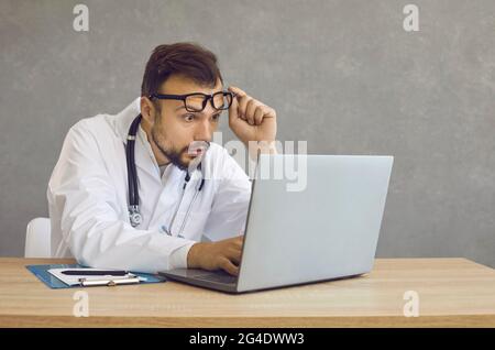 Ein Arzt mit einem schockierten und verwirrten Ausdruck sieht auf einem Laptop-Bildschirm einen medizinischen Fehler. Stockfoto