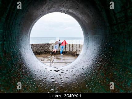 Brighton UK 21. Juni 2021 - starker Regen dämpft heute die Sommersonnenwende am Strand und am Meer von Brighton, während ein Paar mit der Donut-Skulptur dem Wetter trotzt : Credit Simon Dack / Alamy Live News Stockfoto