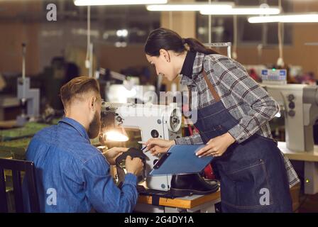 Eine weibliche Qualitätskontrollmanagerin spricht mit einem Schuhmacher am Arbeitsplatz Stockfoto