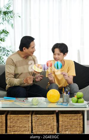 Aufgeregt Vater und Sohn Putting bemalten Kugeln auf Holzstab, um es trocknen zu lassen, wenn das Sonnensystem Modell für die Schule fertig Stockfoto
