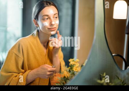 Frau trägt Creme oder Maske auf ihr Gesicht Stockfoto