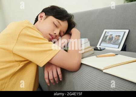 Müder Teenager, der zwischen den Online-Kursen auf einem Bücherstapel schläft Stockfoto