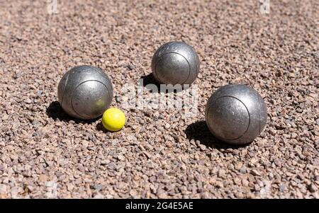 Drei Petanque-Kugeln (Boule) in der Nähe eines gelben Buben zielen auf einen rosa Kiesboden. Stockfoto