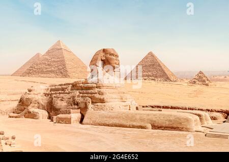 Die große Sphinx mit dem Körper eines Löwen und dem Gesicht eines pharao liegt auf dem Sand vor dem Hintergrund aller berühmten Pyramiden von Gizeh unter einem Stockfoto