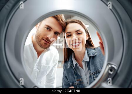 Glückliches Paar, das sich für eine neue Waschmaschine in einem Geschäft entschieden hat, Blick von innen auf die Waschmaschine Stockfoto