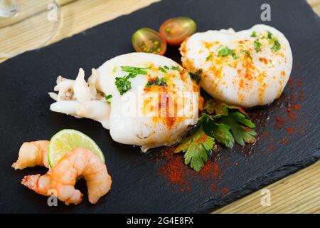 Appetitlich geröstete Cuttlefishes mit würziger Sauce auf Schiefertafel mit gekochten Garnelen, Zitrone und Petersilie serviert. Stockfoto