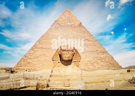 Nahaufnahme des Gesichts der Großen Sphinx mit Pyramide im Hintergrund an einem schönen bewölkten blauen Himmel in Gizeh, Kairo, Ägypten. Vorderansicht Stockfoto