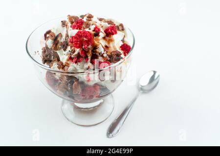 Schokoladeneis mit einer Creme, verschiedenen Nüssen und gefrorenen Beeren auf der Oberseite, in einer Glastasse, isoliert auf weißem Hintergrund Stockfoto