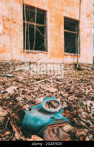 Gasmaske In Der Nähe Des Verlassenen Zerstörten Schulgebäudes Des Alten Dorfes In Der Umsiedlungszone Von Tschernobyl. Weißrussland. Katastrophe Von Tschornobyl. Heruntergekommenes Haus Stockfoto