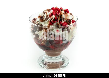 Schokoladeneis mit einer Creme, verschiedenen Nüssen und gefrorenen Beeren auf der Oberseite, in einer Glastasse, isoliert auf weißem Hintergrund Stockfoto