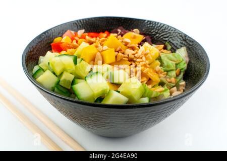 Vegetarischer Poke-Schüssel im schwarzen Design mit Stäbchen unten, isoliert auf weißem Hintergrund. Grüne Gurke, roter Pfeffer, Erdnüsse, Mais, Rote Beete Stockfoto