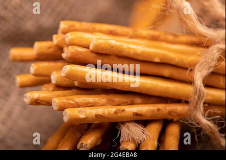 Brotstangen mit Salz, gebunden mit Garn auf dem Hintergrund eines selbstgewebten Stoffes mit einer rauen Textur. Nahaufnahme Selektiver Fokus Stockfoto