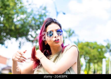 Junge Latina-Frau mit Brille und fuchsiengefärbtem Haar, die ihr Haar mit den Fingern berührte Stockfoto