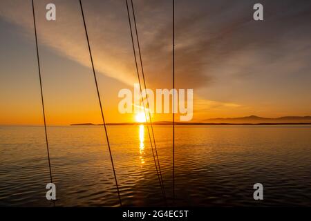 Orange dramatische Sonnenaufgang über dem Meer mit Bank von dunklen Wolken am Himmel durch die Wanten und Seile auf einem Segelboot in Naoussa Village auf Pa gesehen Stockfoto