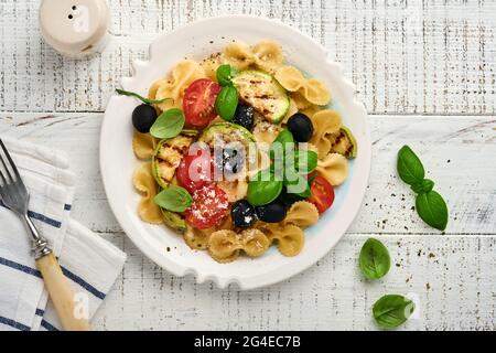 Pasta Fiocchi Salat mit Gemüse gegrillte Zucchini, Kirschtomaten, Oliven, Basilikum und Parmesan in weißem Teller auf hellem Schiefer, Stein oder Beton Stockfoto