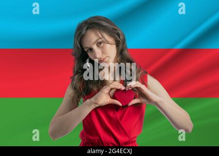 Ich Liebe Aserbaidschan. Ein Mädchen hält vor dem Hintergrund der Flagge Aserbaidschans ein Herz auf ihrer Brust in den Händen. Der Begriff des Patriotismus. Stockfoto