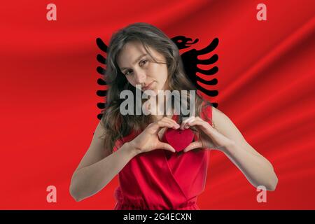 Ich Liebe Albanien. Ein Mädchen hält vor dem Hintergrund der Flagge Albaniens ein Herz auf ihrer Brust in den Händen. Der Begriff des Patriotismus. Stockfoto