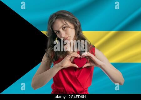 Ich Liebe Bahamas. Ein Mädchen hält vor dem Hintergrund der Flagge der Bahamas ein Herz auf ihrer Brust in den Händen. Der Begriff des Patriotismus. Stockfoto