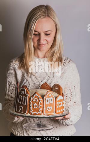 Frau hält hausgemachten Kuchen mit Lebkuchen Stadthaus Fassaden, einen Weihnachtsbaum und Rentiere auf Glasständer Stockfoto